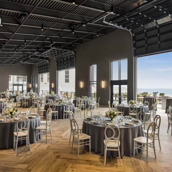 Seaside Vista set in rounds for a wedding reception. The garage doors are open with a direct view of the ocean and the terrace is set with cocktail tables