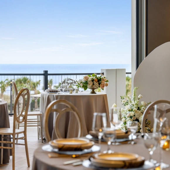 Seaside Vista ballroom set up for a wedding reception. The focus is on the bride and groom table with the ocean in the background