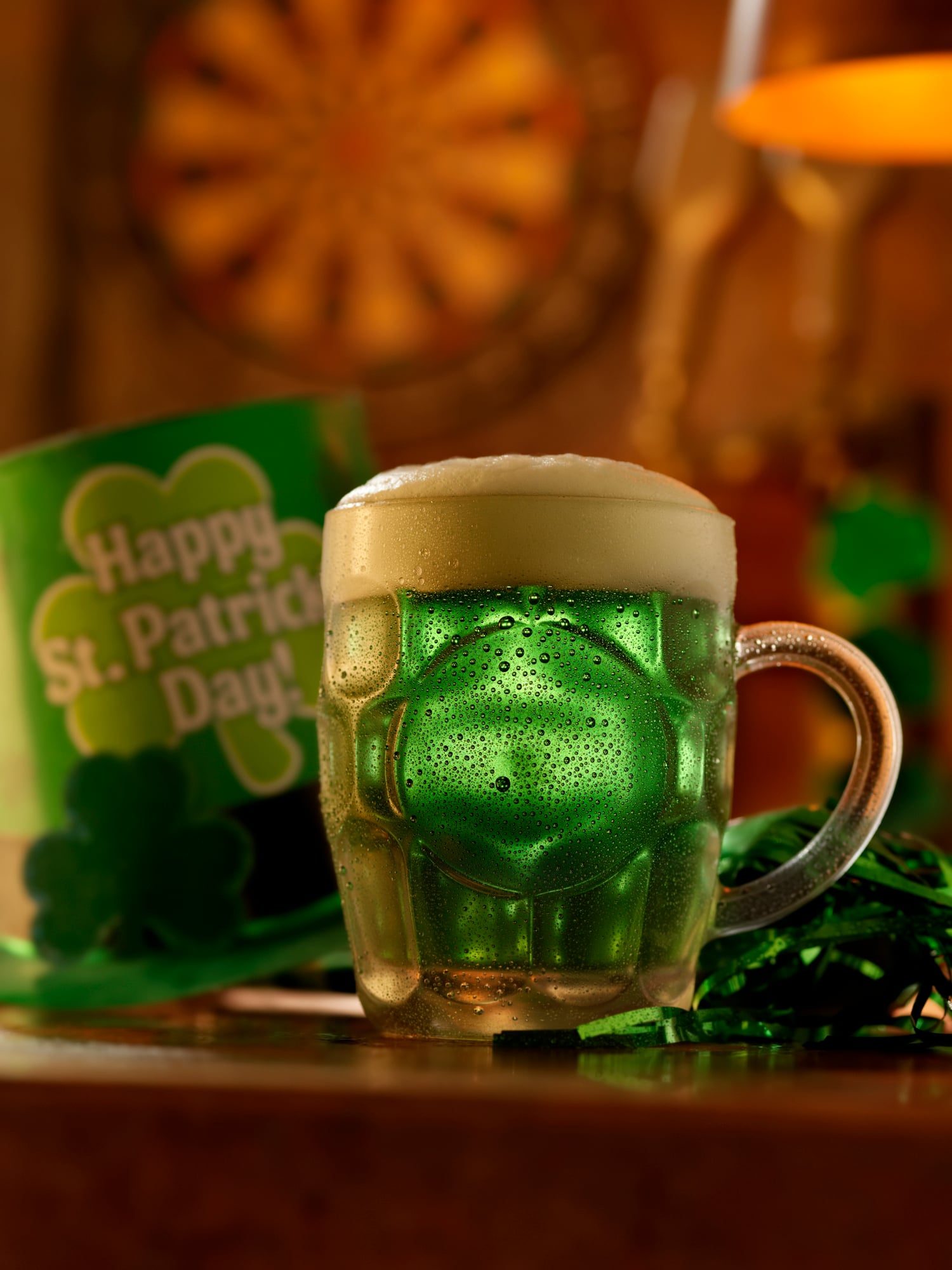 A beer mug full of Green Beer with a sign in the background that says Happy St. Patrick's Day!