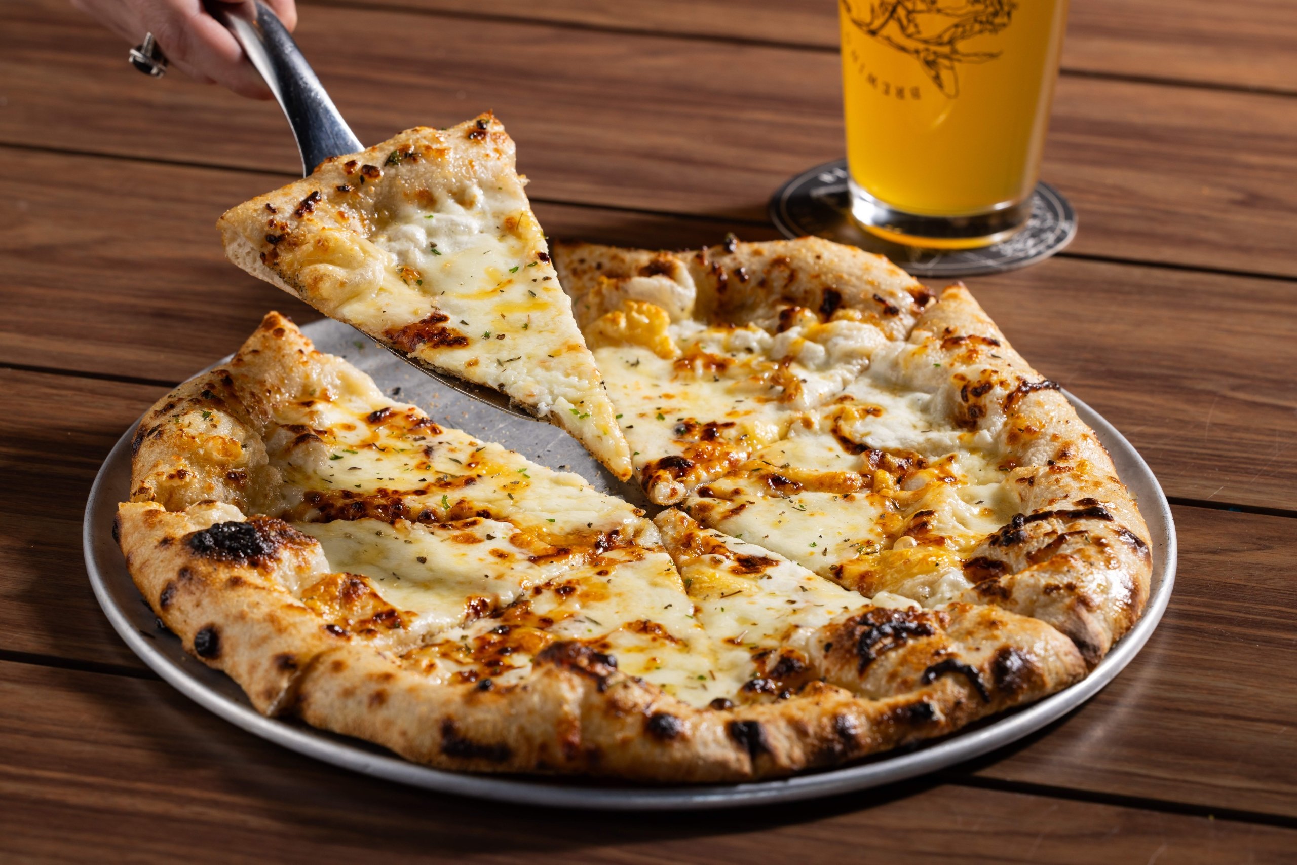 Black Drum Brewing's Honeysuckle pizza with a slice being picked up and a beer in the background