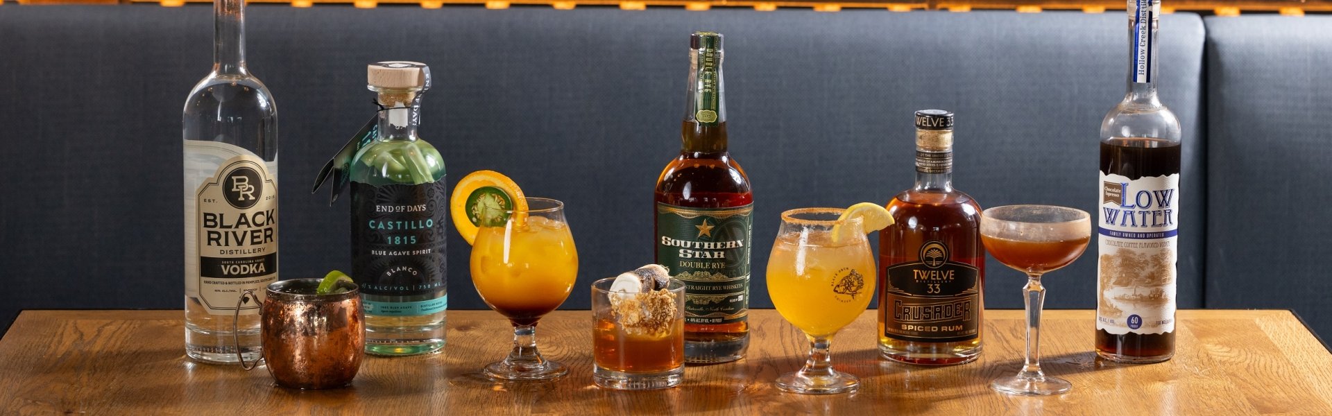 Six cocktails in varied glasses with their liquor bottles next to them